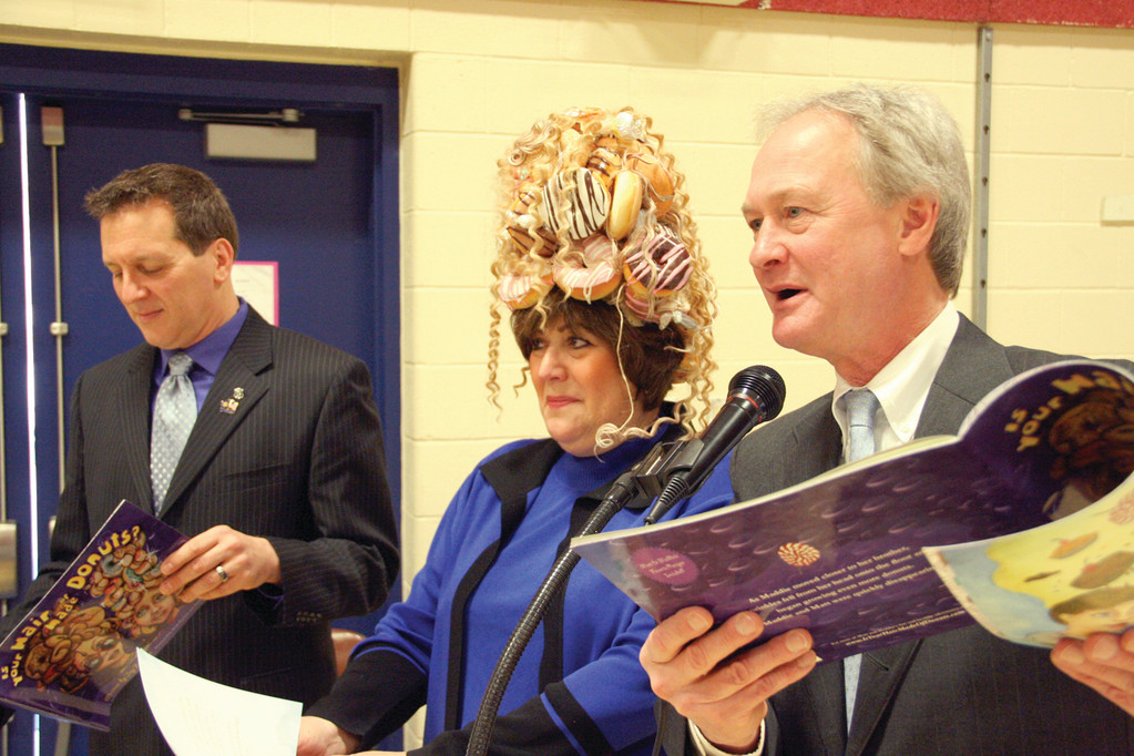 OH SO GOOEY: Eva Marie Mancuso, chair of the state Board of Education, wears the donut hat as Gov. Chafee reads from Feldman’s book and Rep. Frank Ferri awaits his turn recently at John Wickes School.