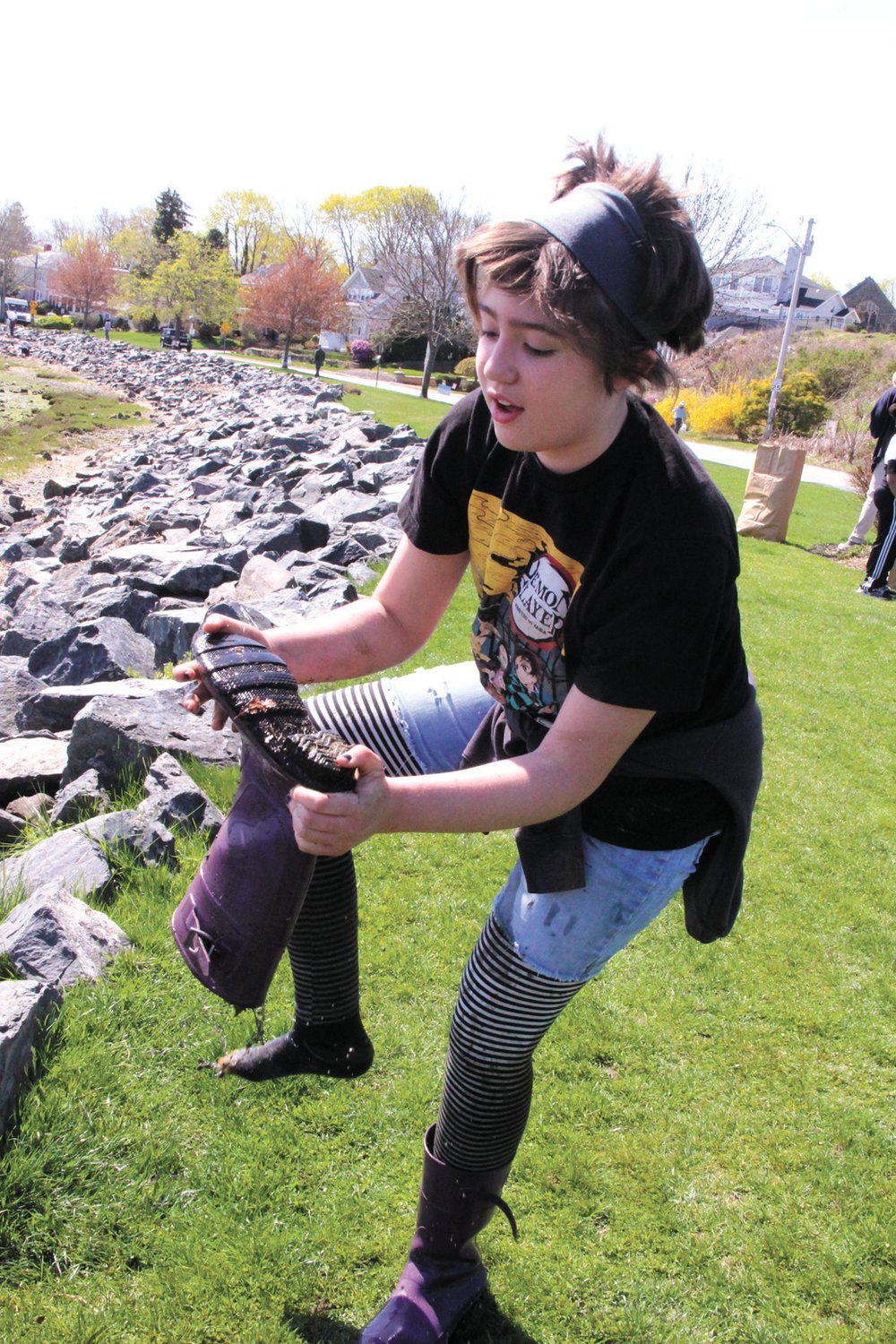 Out of the muck: Hazel Robinson empties her boots of water after becoming stuck in the mud along with another young woman Saturday during the Stillhouse Cove salt marsh and park cleanup Saturday. Hazel was not perturbed by the incident, noting this is the third year in a row that it’s happened to her during the cleanup.  (Cranston Herald photos)